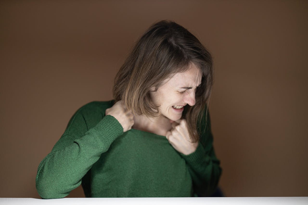 Portrait of a woman expressing strong emotion, wearing a green sweater against a brown background.