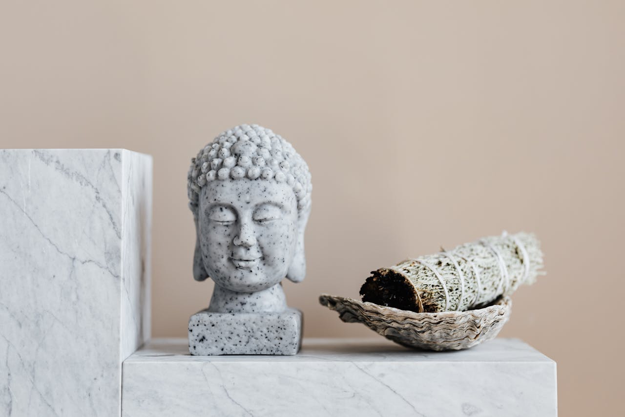 Buddha sculpture and sage bundle on marble blocks, symbolizing peace and meditation.