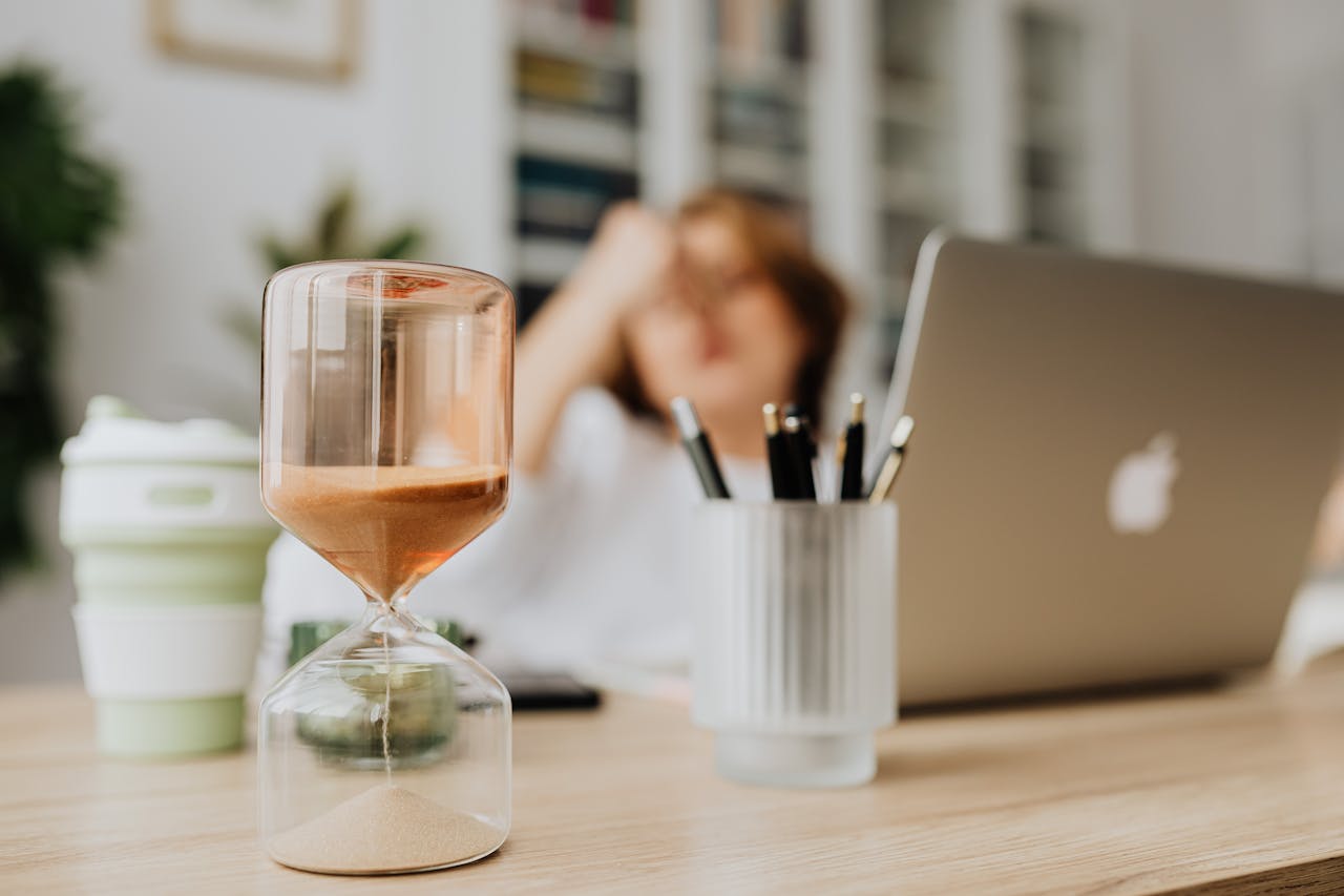 A focused hourglass on a desk with a laptop in an office setting, highlighting time management.