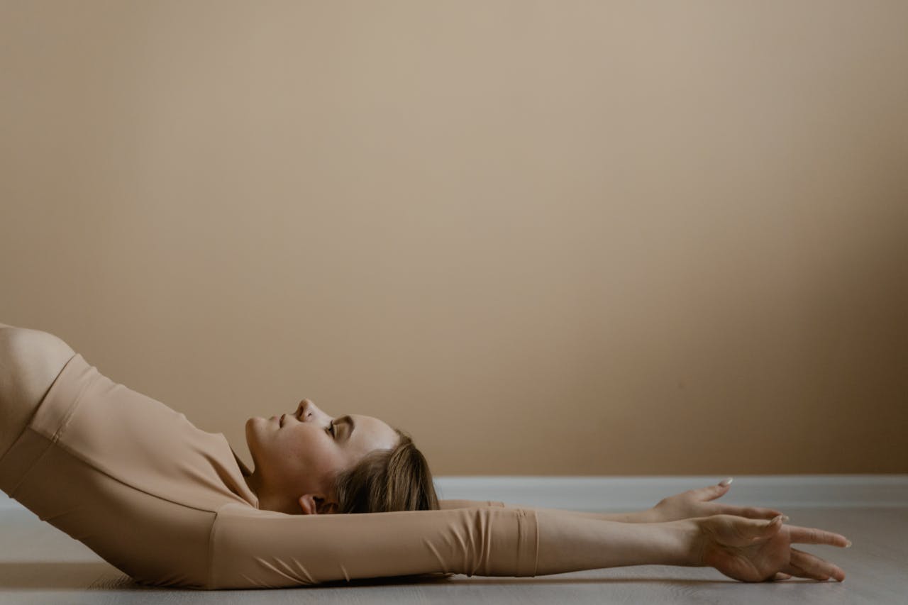 Woman in calm yoga pose, arms extended, in neutral setting.